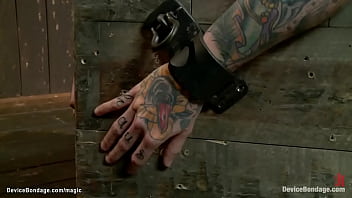 Tattooed lesbian slave Kathryn Dupri on back on wooden box shackled and face bound in wire caned then bound in leather spanked on the floor in dungeon by lezdom Claire Adams